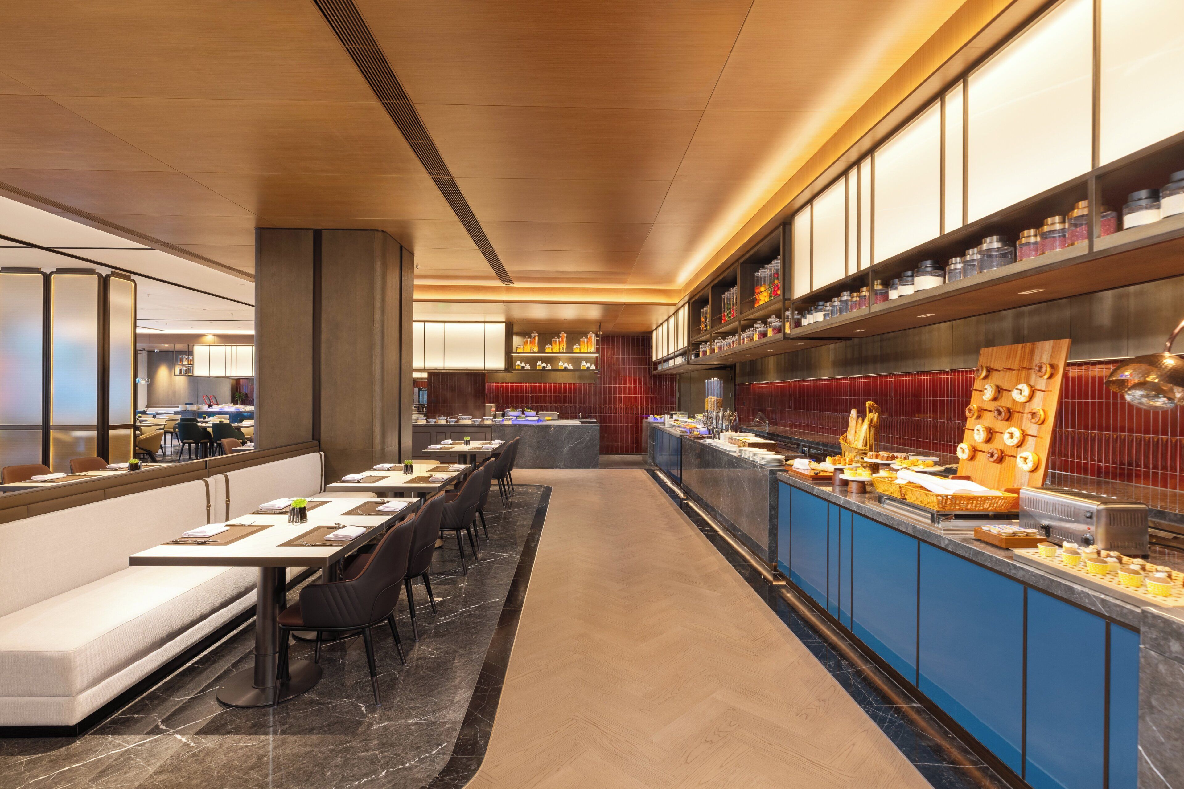 Un restaurante moderno con una barra larga, zona de estar y cocina al fondo.