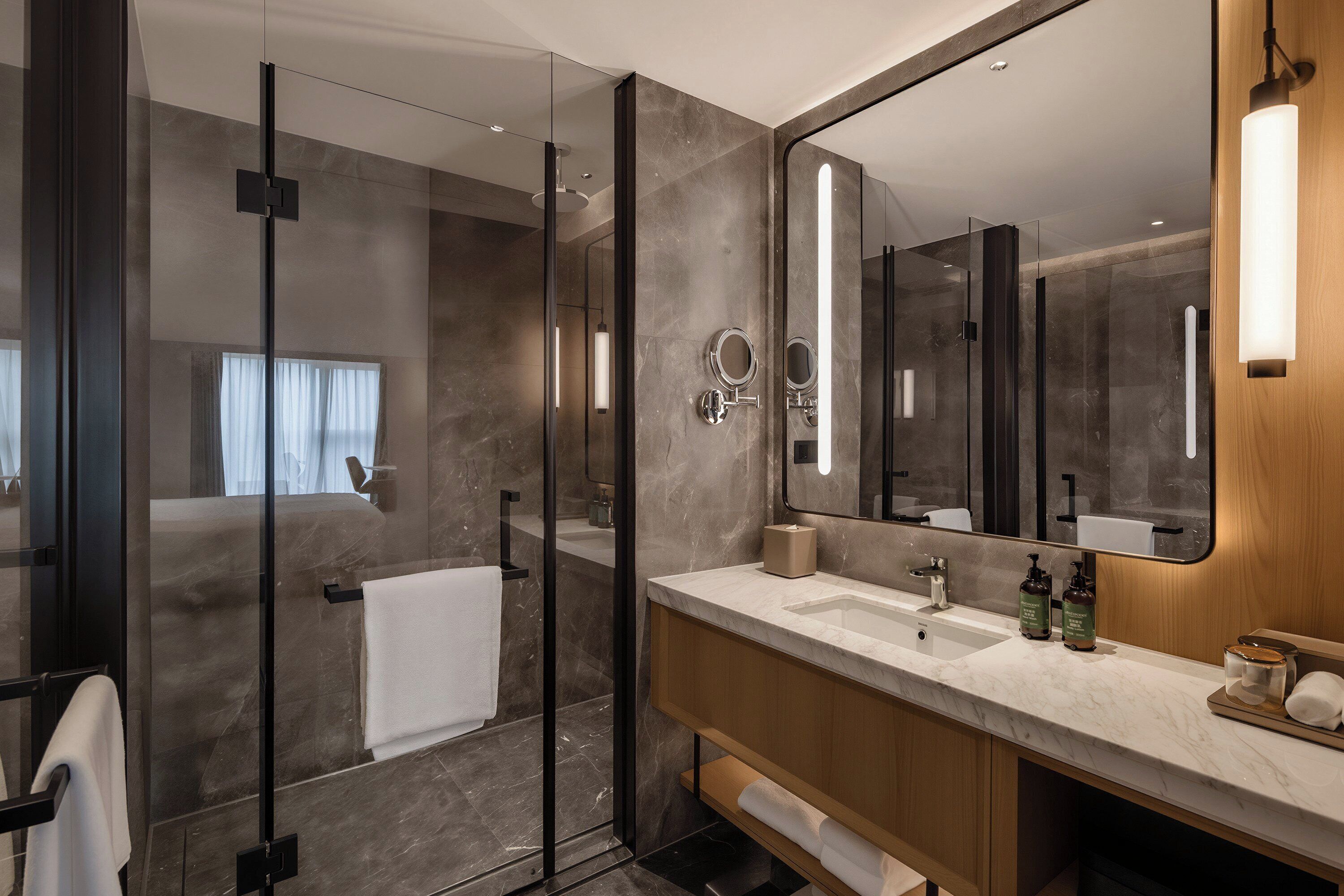 A modern bathroom with a glass shower enclosure, a large mirror, and a marble countertop.