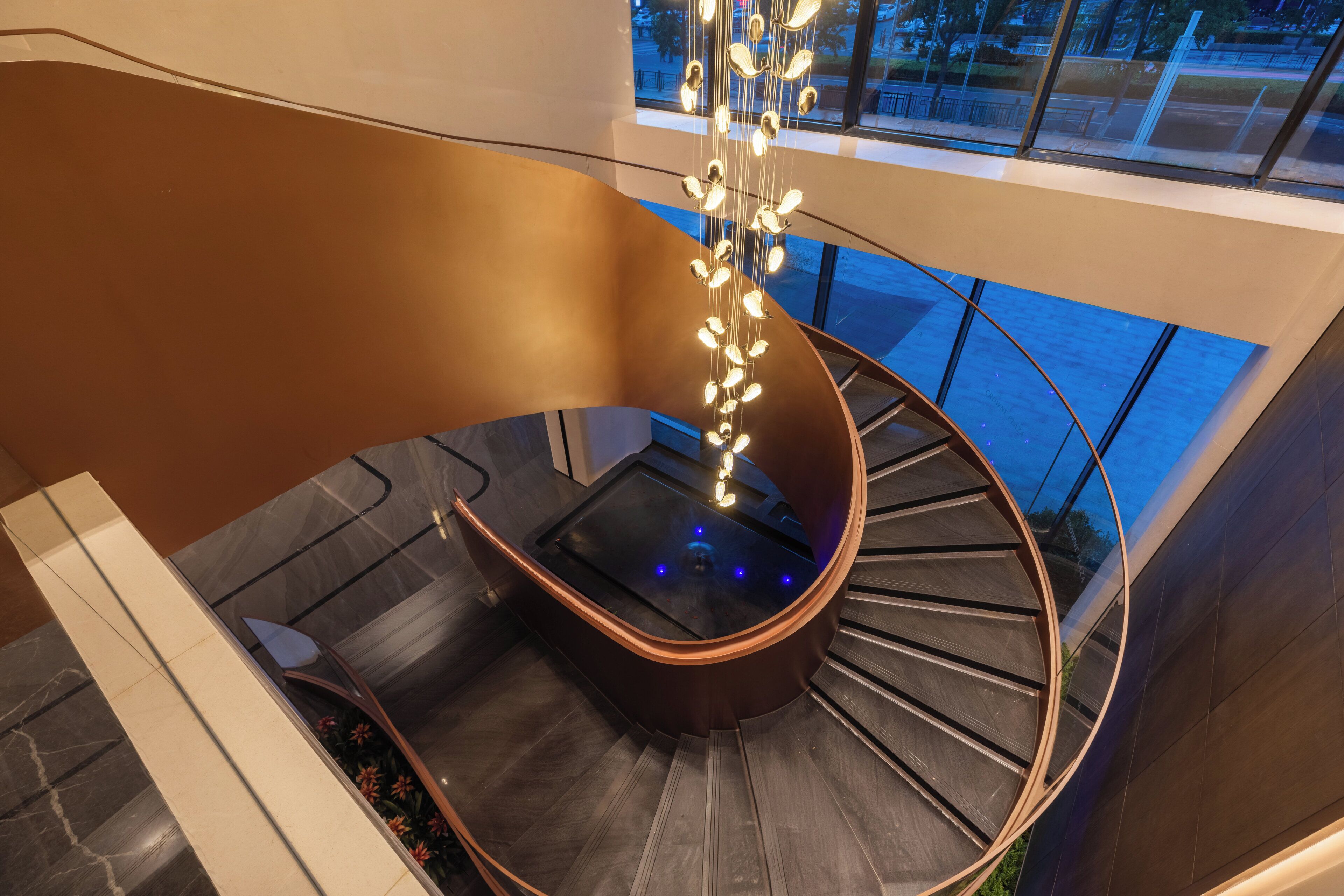 Un escalier en colimaçon moderne, doté d’une rampe en verre et d’un luminaire original.