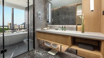 A modern bathroom with a large mirror, a bathtub, and a view of the city.