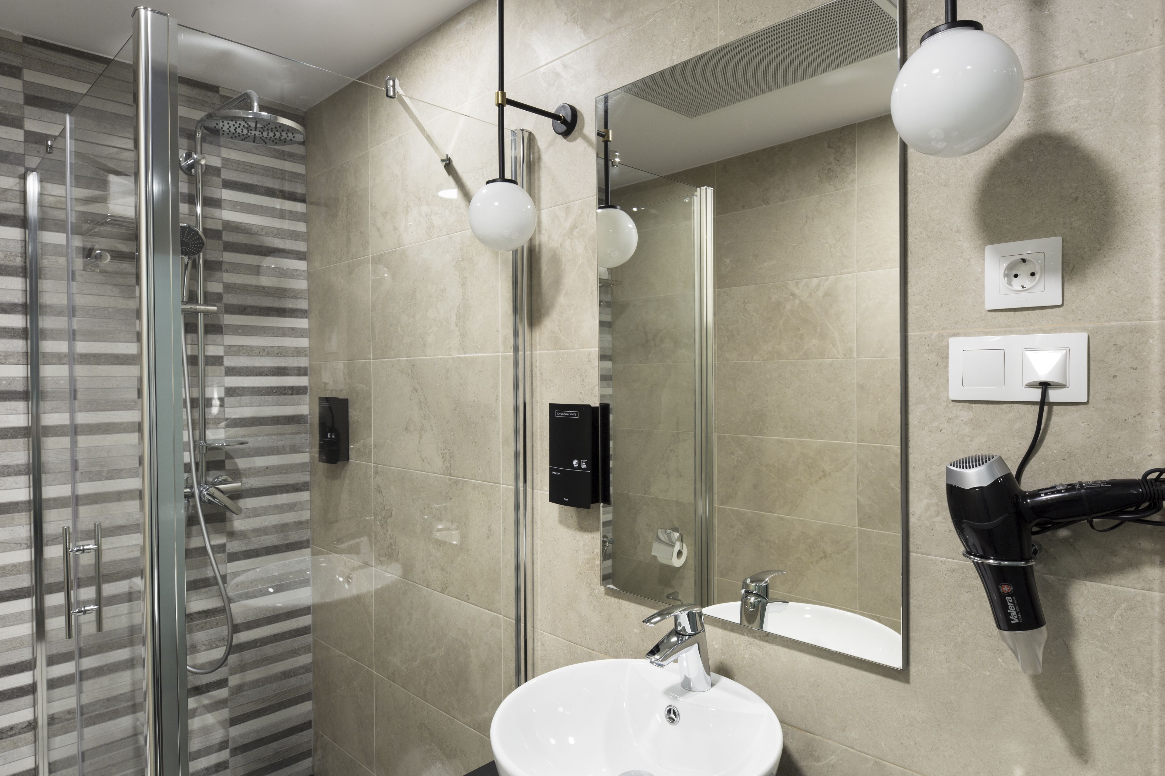 A modern bathroom with a glass shower enclosure, a white sink, and a hairdryer mounted on the wall.
