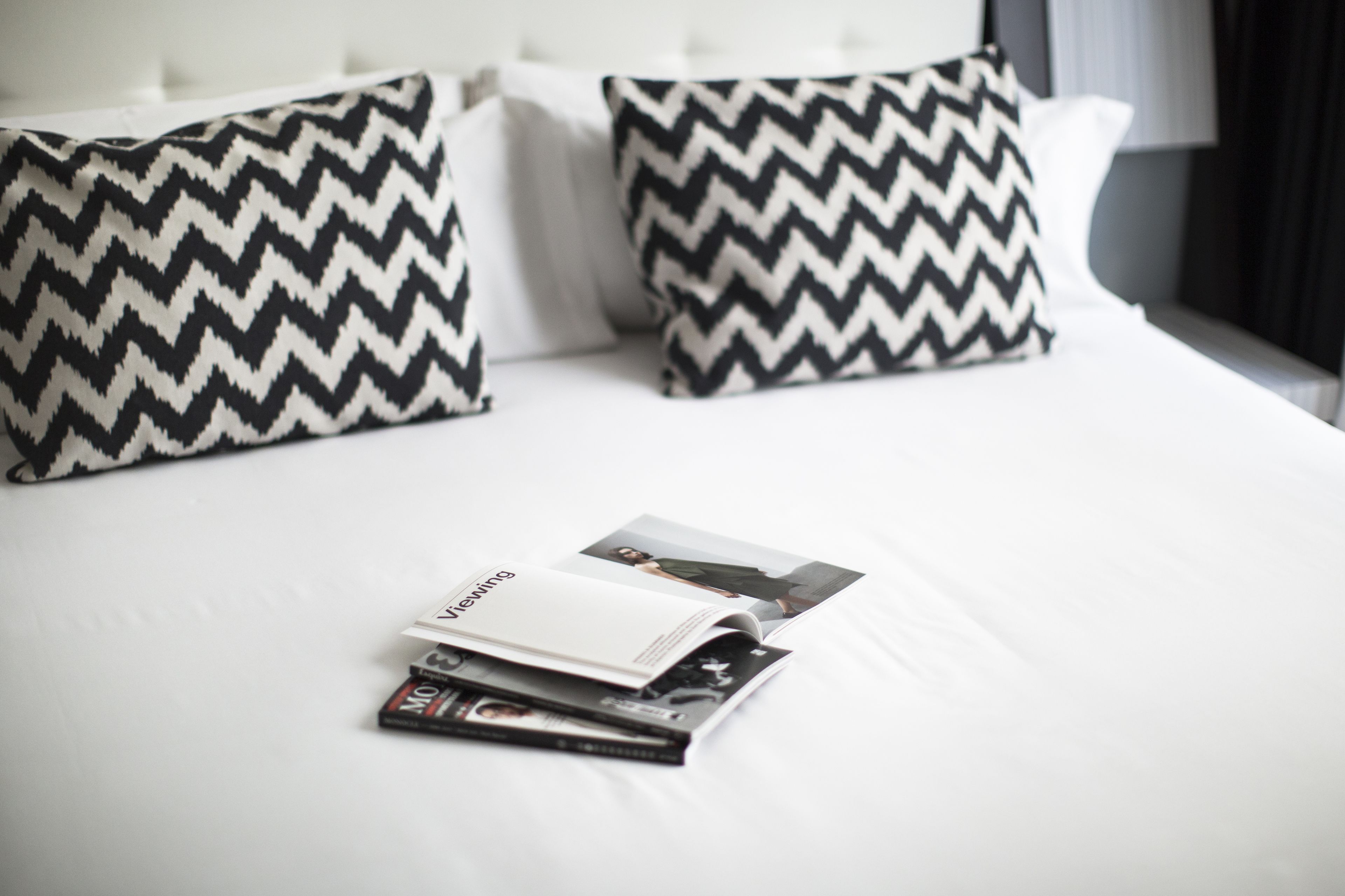 A neatly made bed with two black and white zigzag patterned pillows and a magazine on the bed.