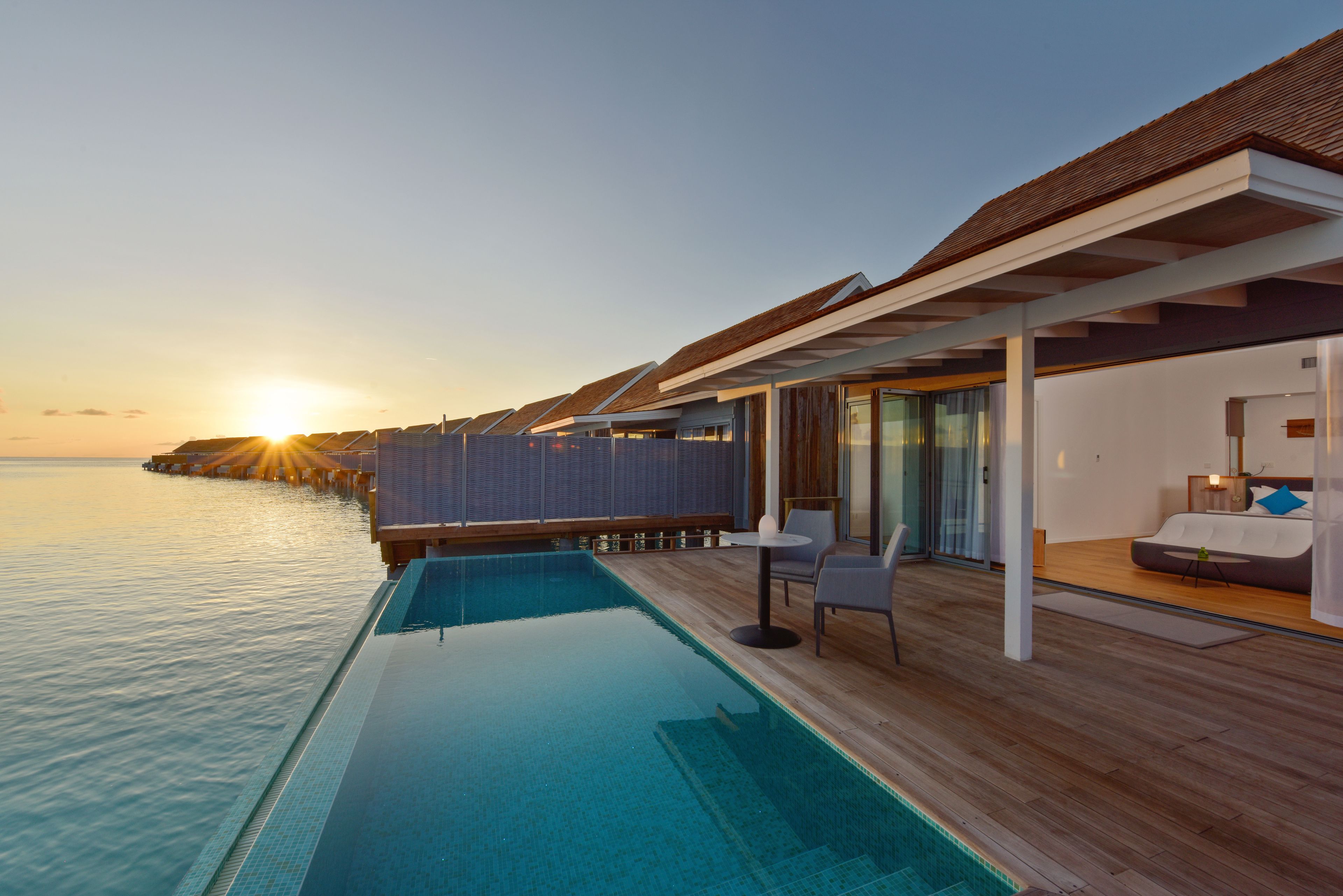 Una piscina infinita con terraza de madera, con vista al mar al atardecer.