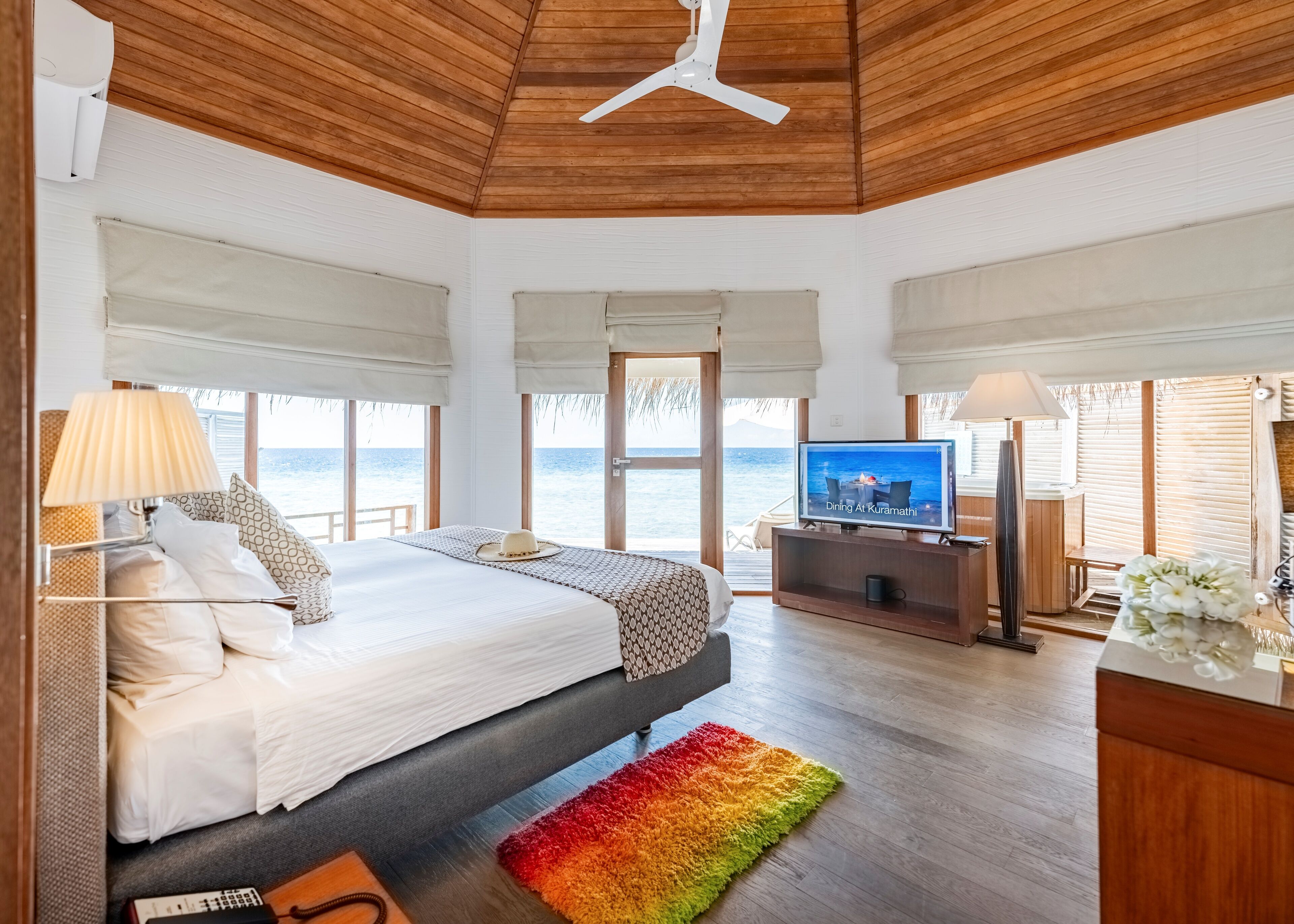 A bedroom with a bed, a TV, a desk, and a view of the sea.