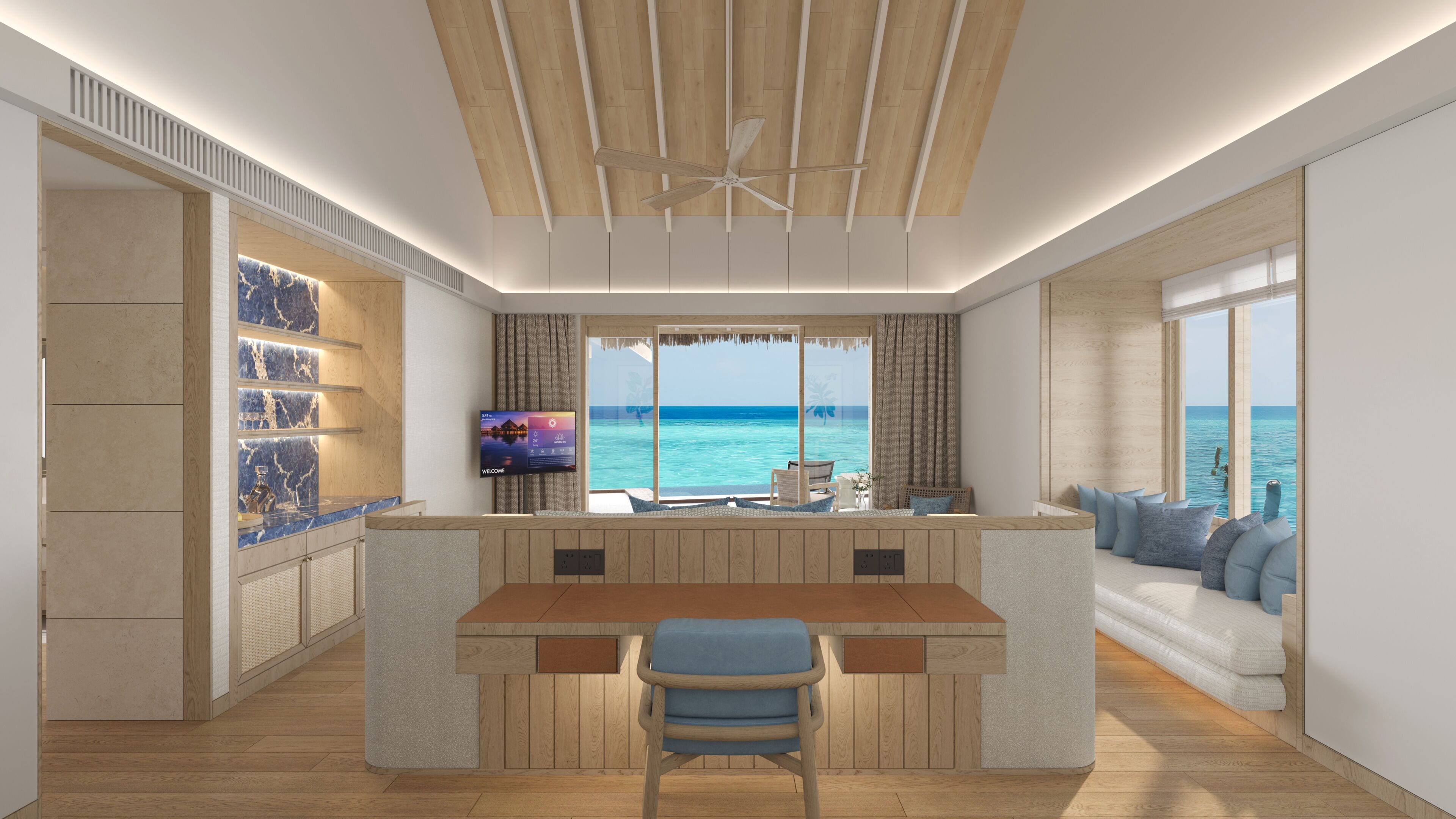 A modern kitchen with a central island, a seating area with a view of the sea, and a television on the wall.