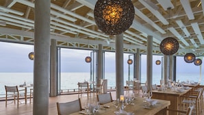 A dining area with tables set for a meal, large windows overlooking the sea, and hanging spherical light fixtures. - Niva Kuramathi Maldives (Kuramathi Island)