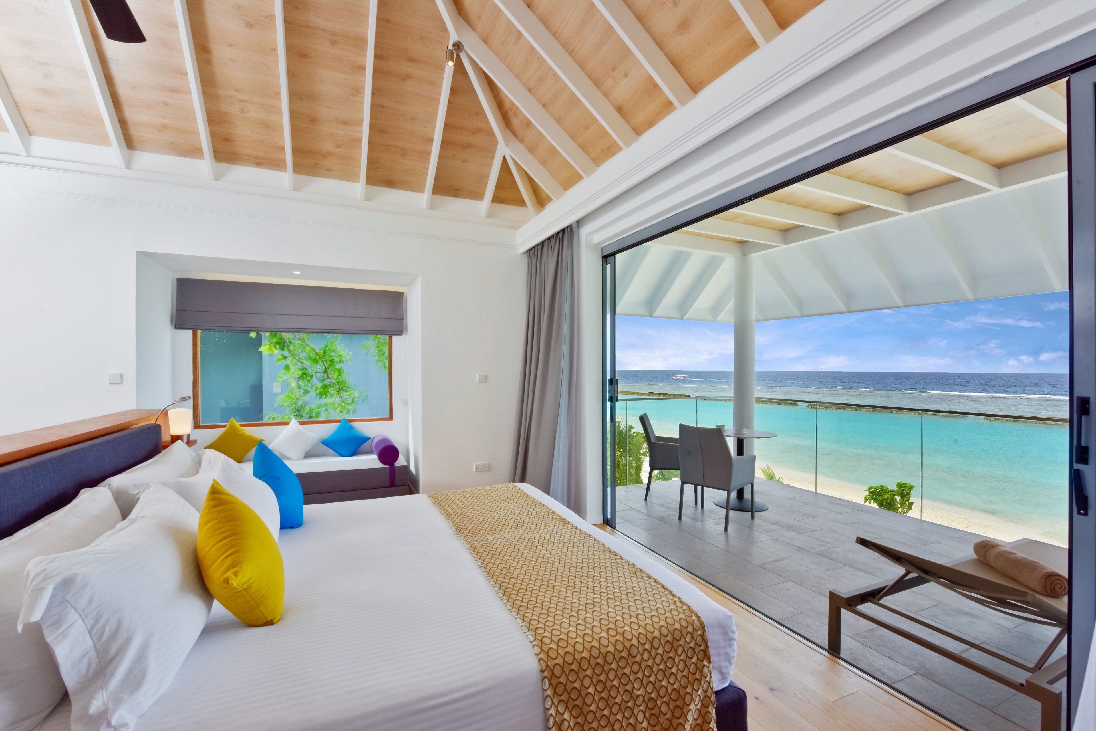 Un dormitorio con una cama grande, vista al océano y un balcón con mesa y sillas.