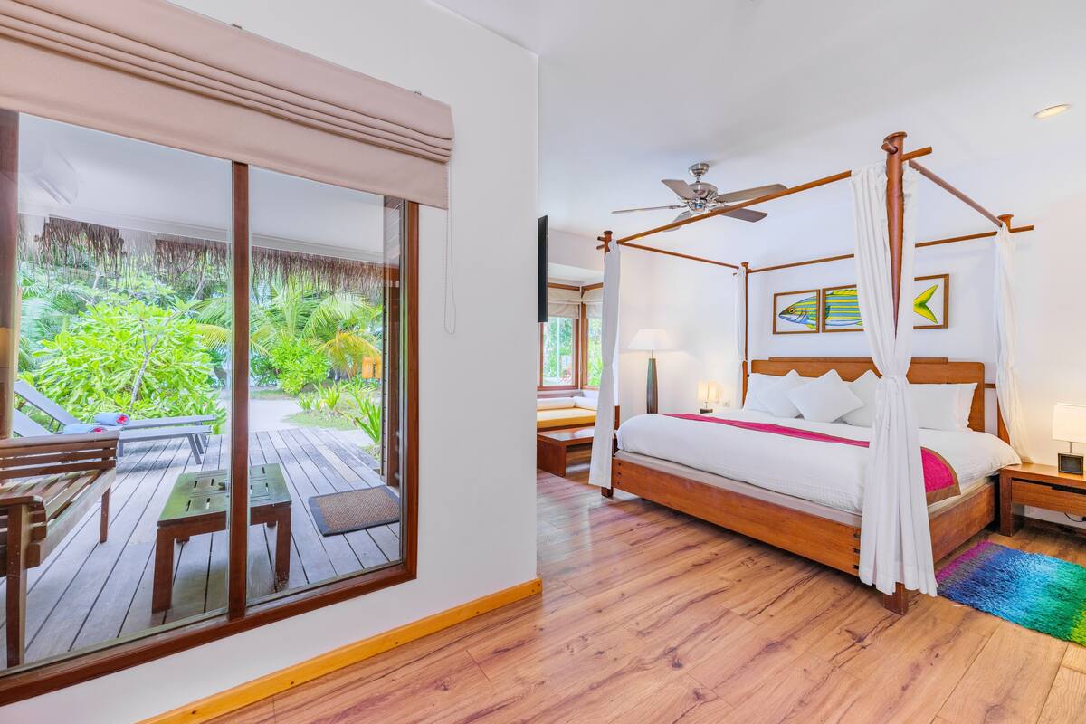 Un dormitorio con cama con dosel, ventilador de techo y vistas a un jardín exuberante a través de amplios ventanales correderas.