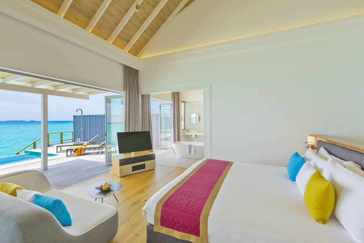 Una habitación de hotel moderna con una cama grande, televisión, balcón con piscina y vista al océano.