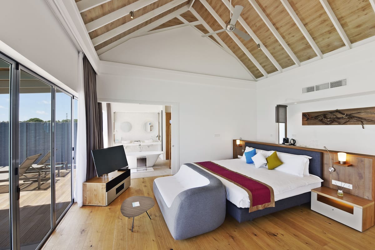 Un dormitorio moderno con una cama grande, un televisor, un escritorio y un balcón con sillones de sol.