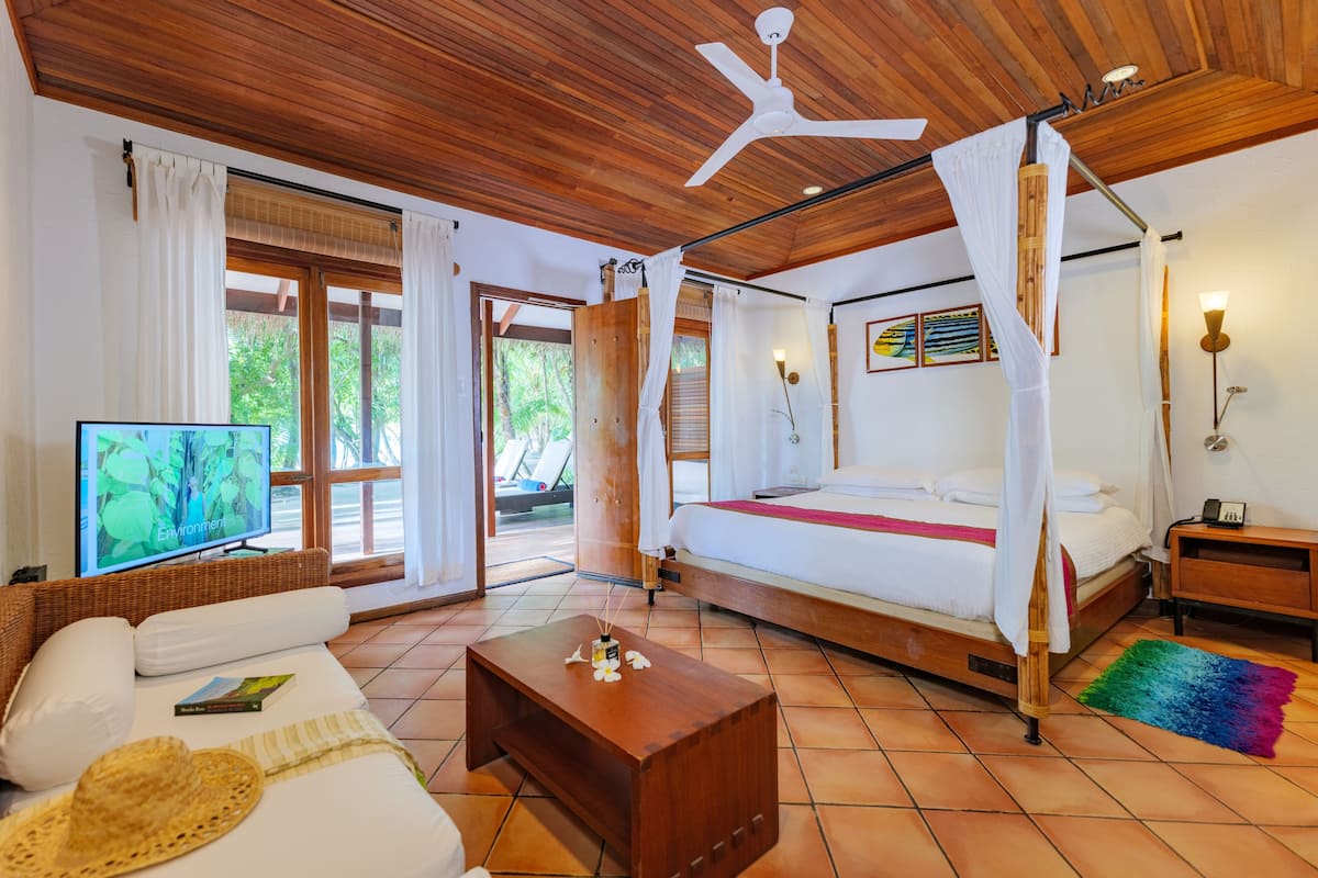 Una habitación con cama, televisión, techo de madera y vista a zonas verdes.