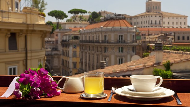 A table with a cup of tea, a teapot, and a bouquet of flowers on a balcony overlooking historic buildings. - La Fenice (Rome)