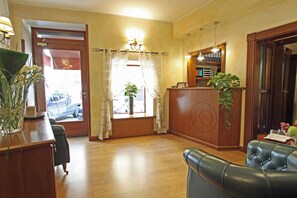 A hotel lobby with a reception desk, a leather sofa, a wooden reception desk, a potted plant, and a window with curtains. - La Fenice (Rome)