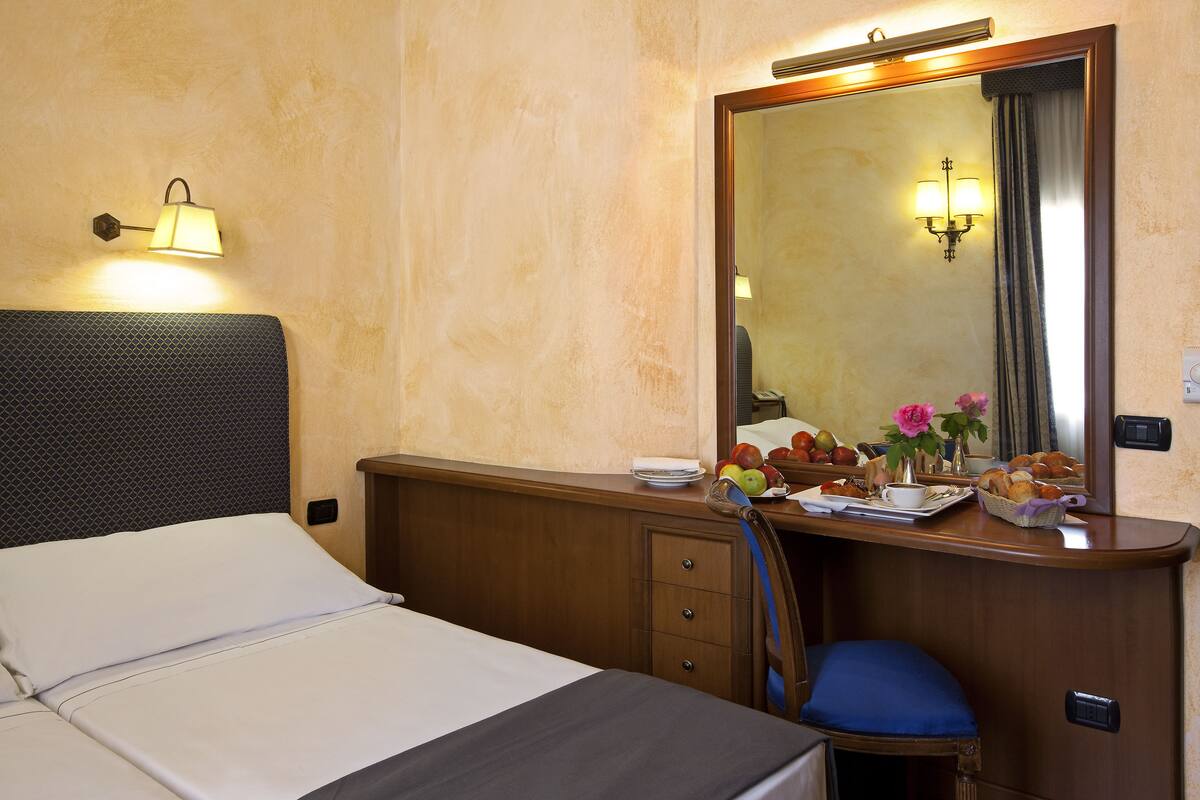 A hotel room with a bed, a wooden dresser, a mirror, and a nightstand.