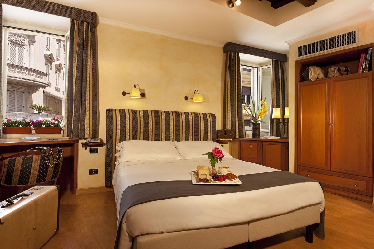 A hotel room with a bed, bedside table, lamp, and a view of the outside balcony.