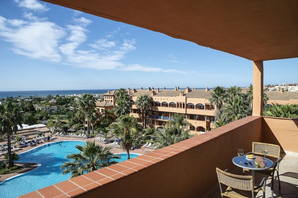 A poolside view with a clear view of the ocean, a pool, and a building with multiple balconies. - Pierre & Vacances Estepona (Benahavis)