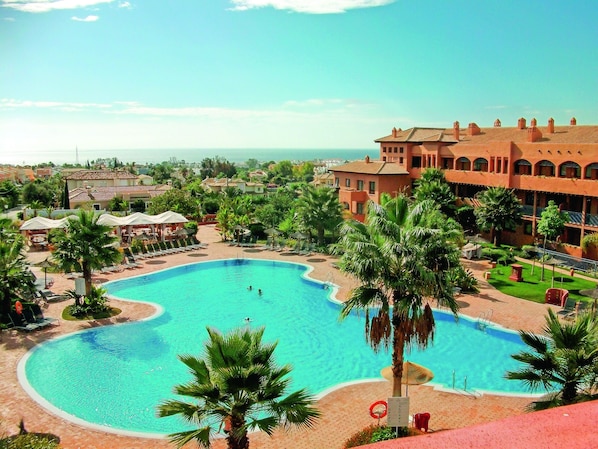 A large swimming pool with palm trees, lounge chairs, and a building with multiple balconies in the background. - Pierre & Vacances Estepona (Benahavis)