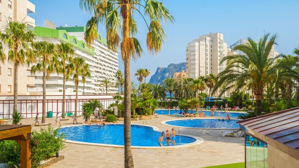 A hotel with multiple swimming pools, palm trees, and a mountainous backdrop. - Apartamentos Coral Beach (Calpe)
