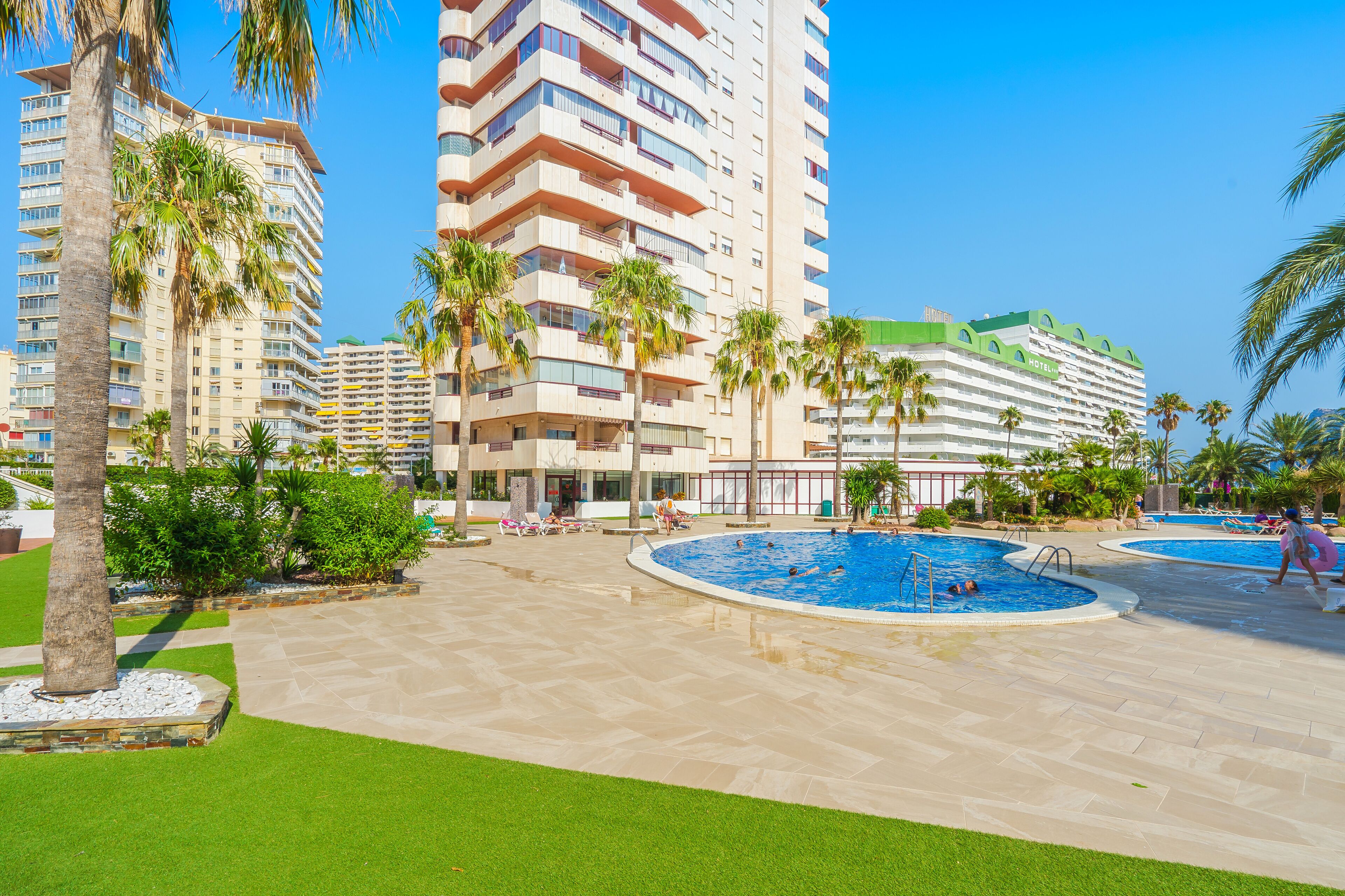 Un hotel de varios pisos, piscina y palmeras.