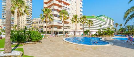 Un hotel de varios pisos, piscina y palmeras.