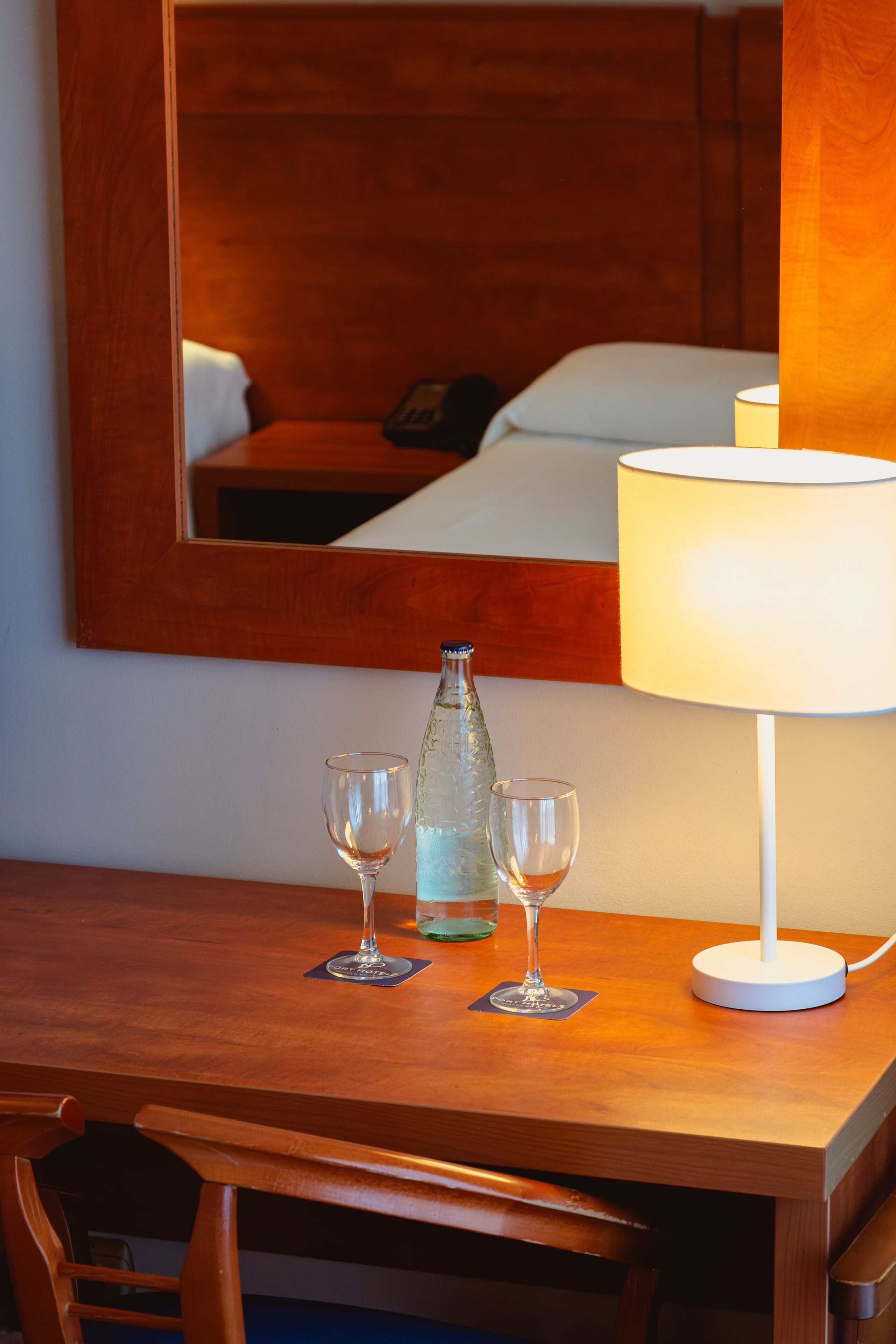 A wooden desk with a bottle, two glasses, and a white lamp.
