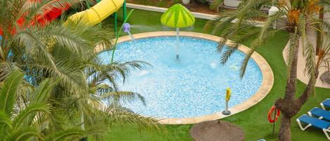 Piscina con tobogán, rodeada de palmeras y sillas de descanso azules.