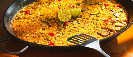 A large, shallow cooking pan filled with a yellow rice dish, garnished with lime slices and a black spatula.