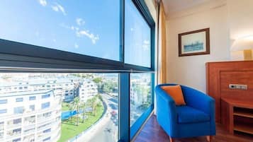 A room with a large window offering a view of a cityscape, a blue armchair, and a wooden cabinet.