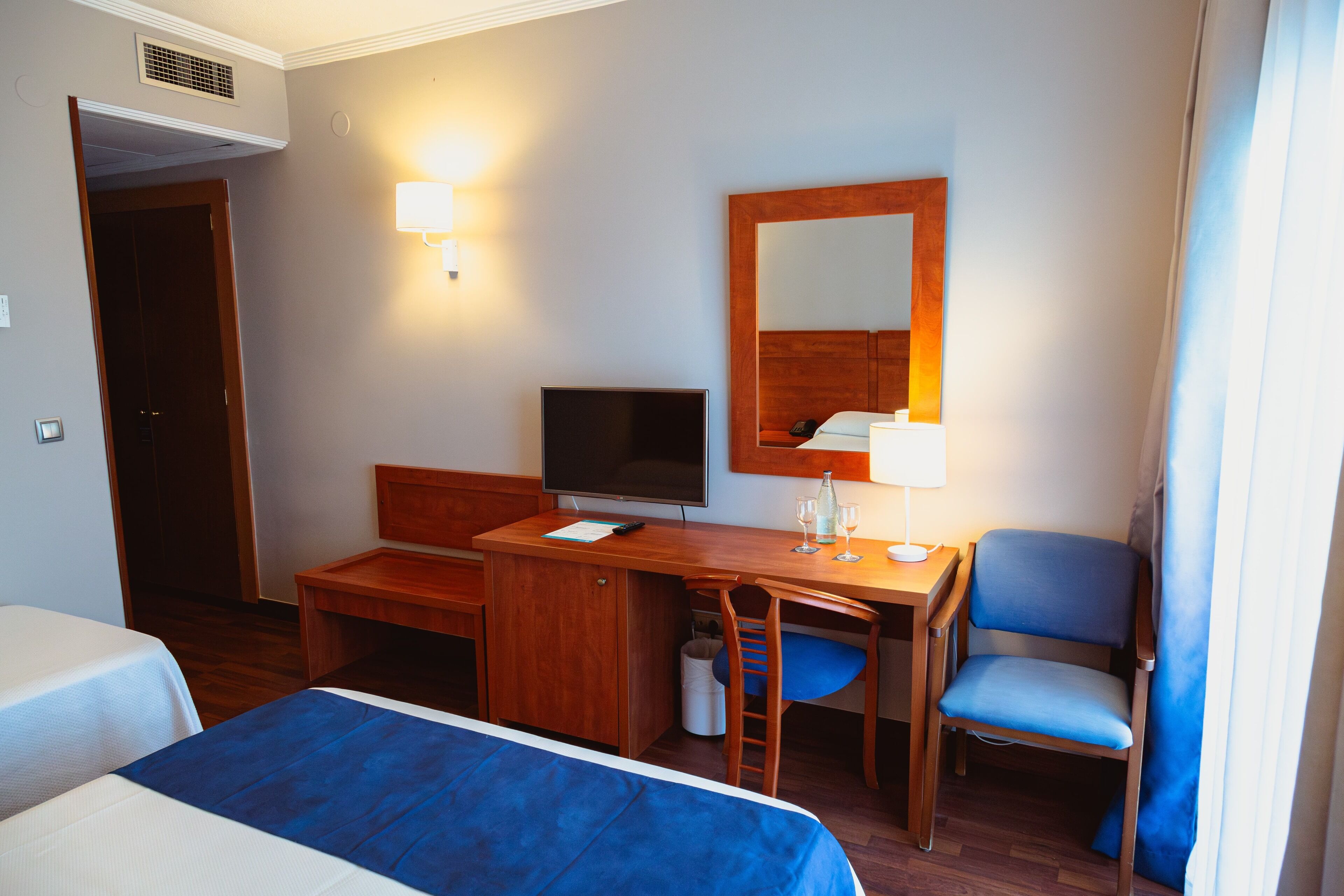 A hotel room with a bed, a desk, a chair, a television, and a mirror.