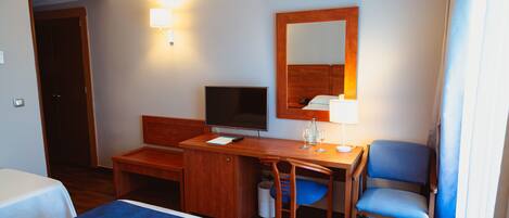A hotel room with a bed, a desk, a chair, a television, and a mirror.