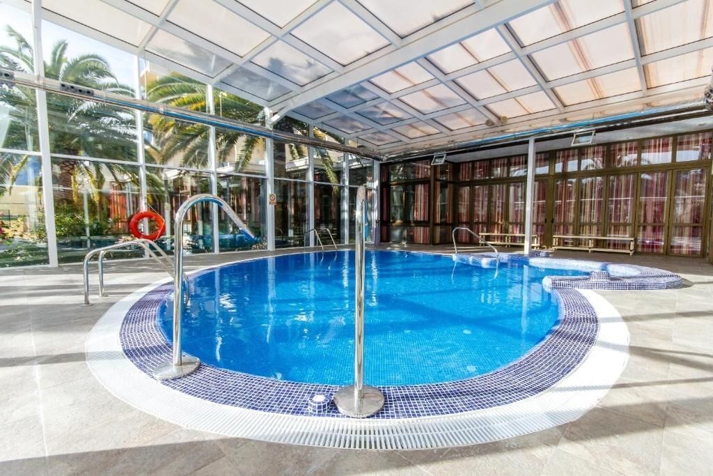 An indoor swimming pool with clear glass walls, a tiled edge, and a lifeguard chair.