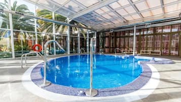 Una piscina interior con paredes de vidrio transparente, borde de azulejos y una silla para socorrista.