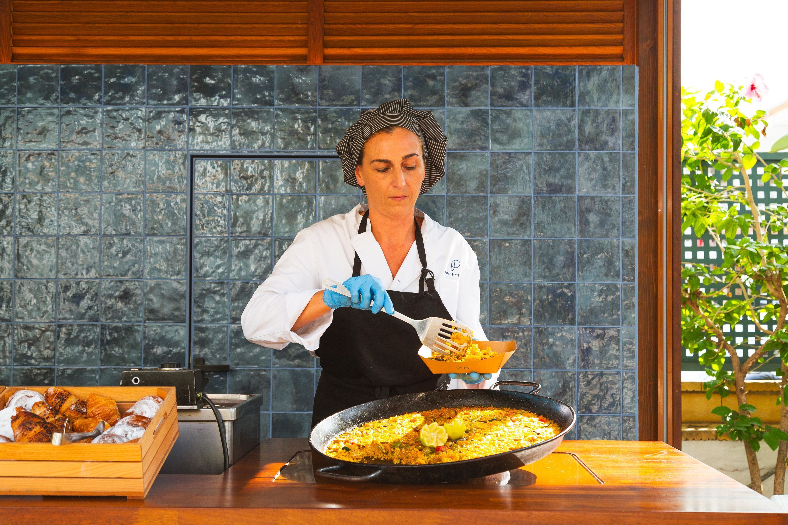 Un chef preparando una gran sartén de comida en una cocina con salpicadero de azulejos y encimera de madera.