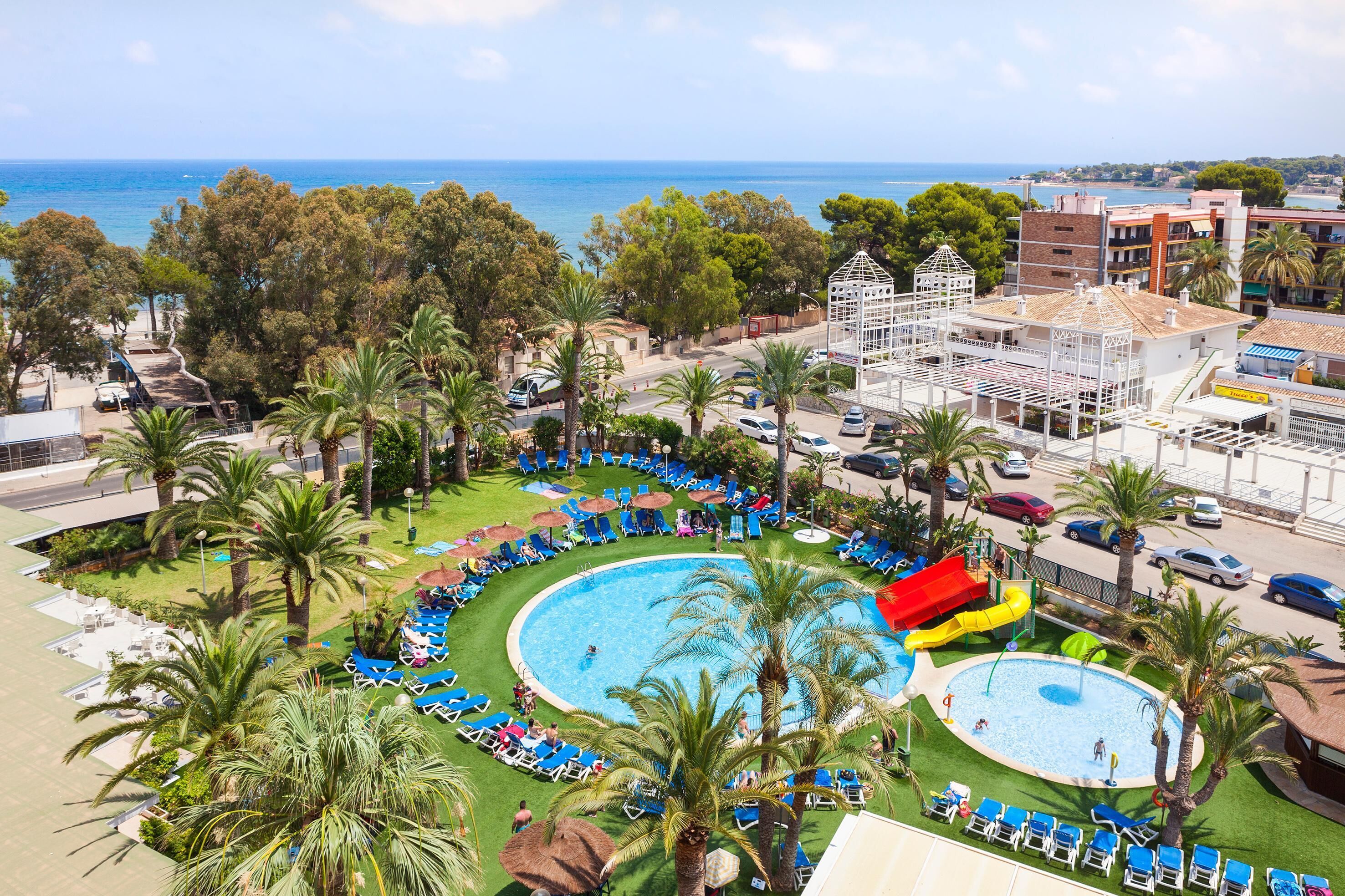 A resort with a large pool, palm trees, and a view of the sea.