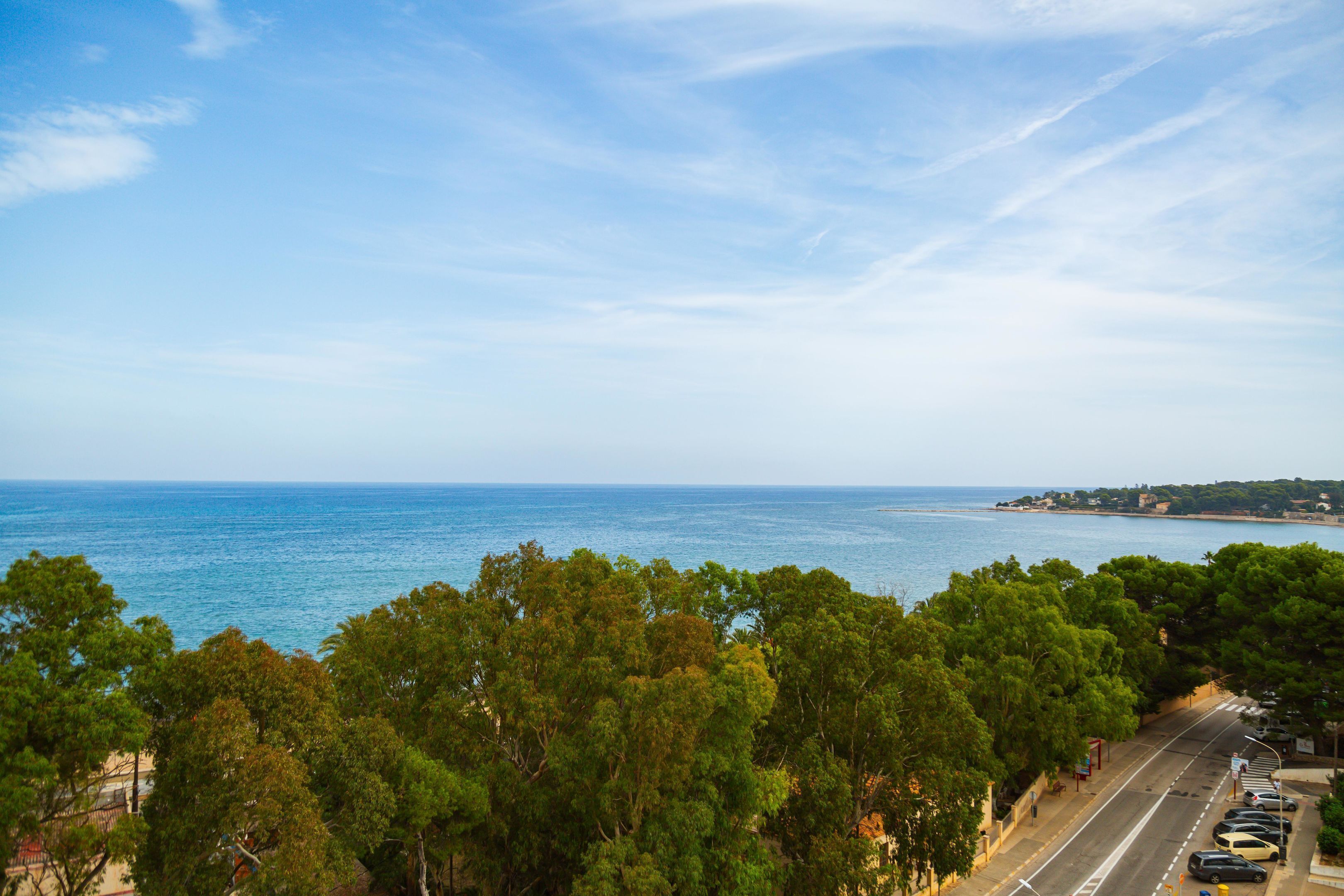 Eine Küstenstraße mit parkenden Autos, dichtem Grün und freiem Blick auf das Meer.