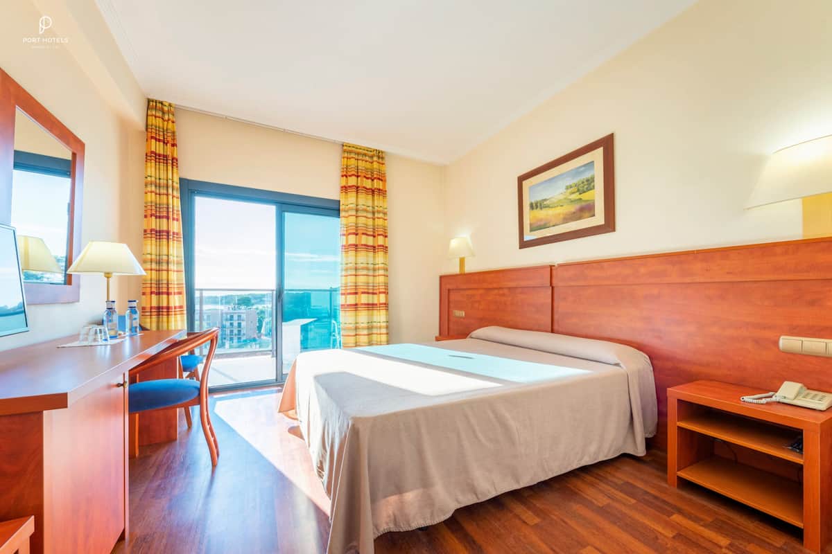 A hotel room with a large bed, a desk with a chair, a small table, and a view of the city.