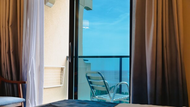 Una habitación de hotel con una cama, una silla y un balcón con una butaca.