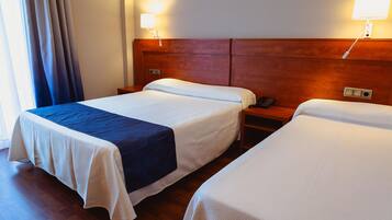 A hotel room with two beds, wooden headboards, bedside lamps, a telephone, and a window with curtains.