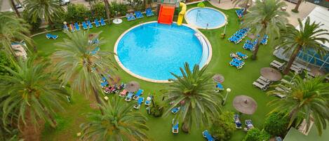 A large outdoor swimming pool surrounded by palm trees and lounge chairs.