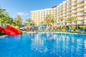 A hotel with a swimming pool, palm trees, and a red slide.