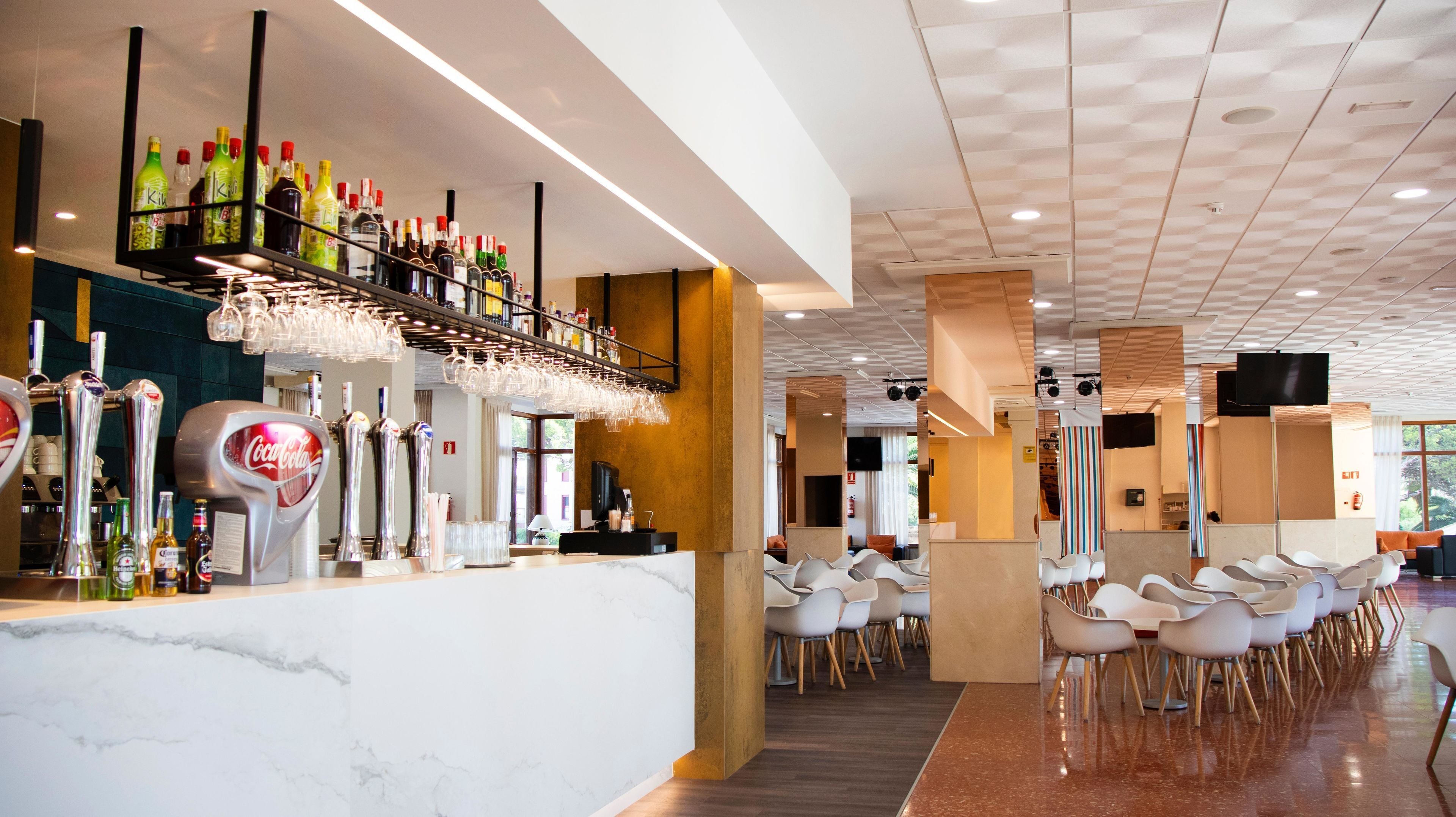 A modern bar area with a variety of liquor bottles, a Coca-Cola dispenser, and a glassware rack.