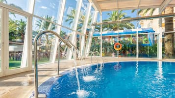 Una piscina interior con paredes de vidrio transparente, suelo de baldosas y un flotador.