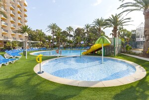 A swimming pool with a slide, surrounded by blue lounge chairs and palm trees.