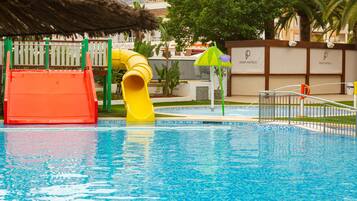 Une piscine avec un toboggan, un parasol en chaume et une clôture avec des panneaux indicateurs.