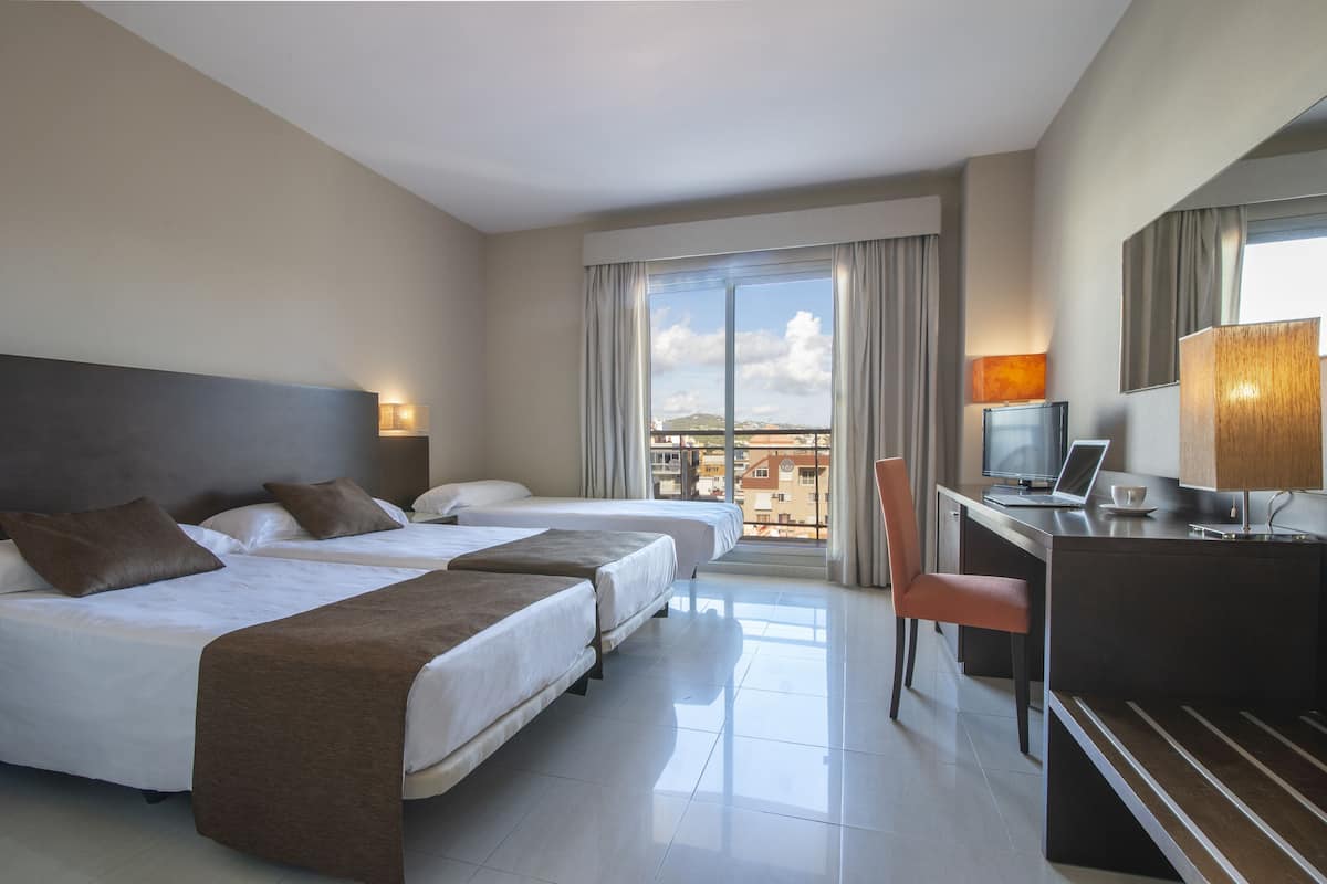 A hotel room with two beds, a desk, a chair, and a large window with a city view.