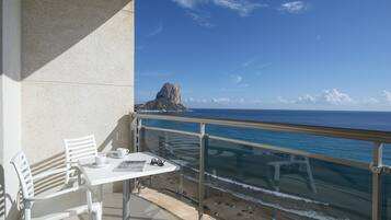 A balcony with a table and chairs overlooking a beach and a rocky outcrop.