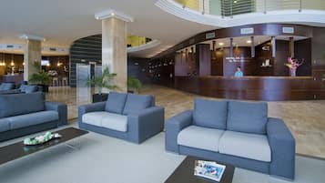Un vestíbulo amplio con mobiliario moderno, una recepción y una escalera que sube a un nivel superior.