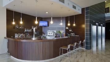 Een moderne bar met een gebogen toonbank, hangende pendelverlichting, een flatscreen-tv en barstoelen.