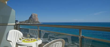 A balcony with a table set for two, overlooking a beach and a rocky outcrop.