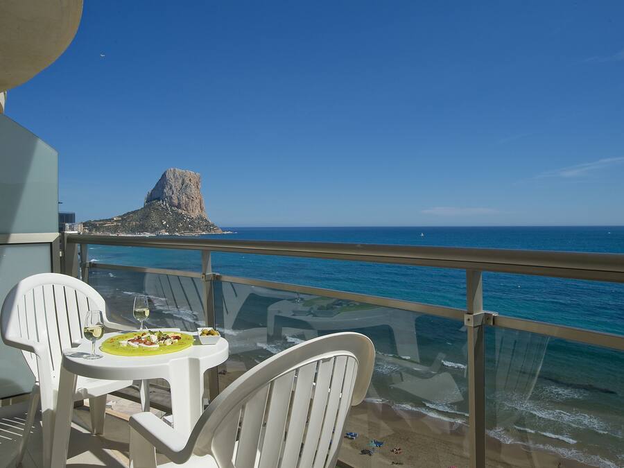 Een balkon met een tafel gedekt voor twee, met uitzicht op een strand en een rotsformatie.